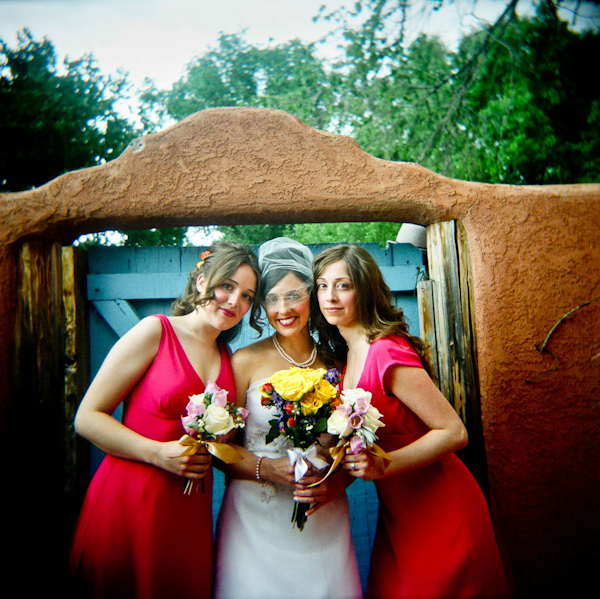 beautiful bride with her two bridesmaids wearing a white a-line dress and birdcage veil holding a yellow, dark pink, purple, and green bouquet while bridesmaids are wearing dark pink dresses and holding ivory and light pink, and lavendar bouquets - photo by New Mexico based wedding photographers Twin Lens